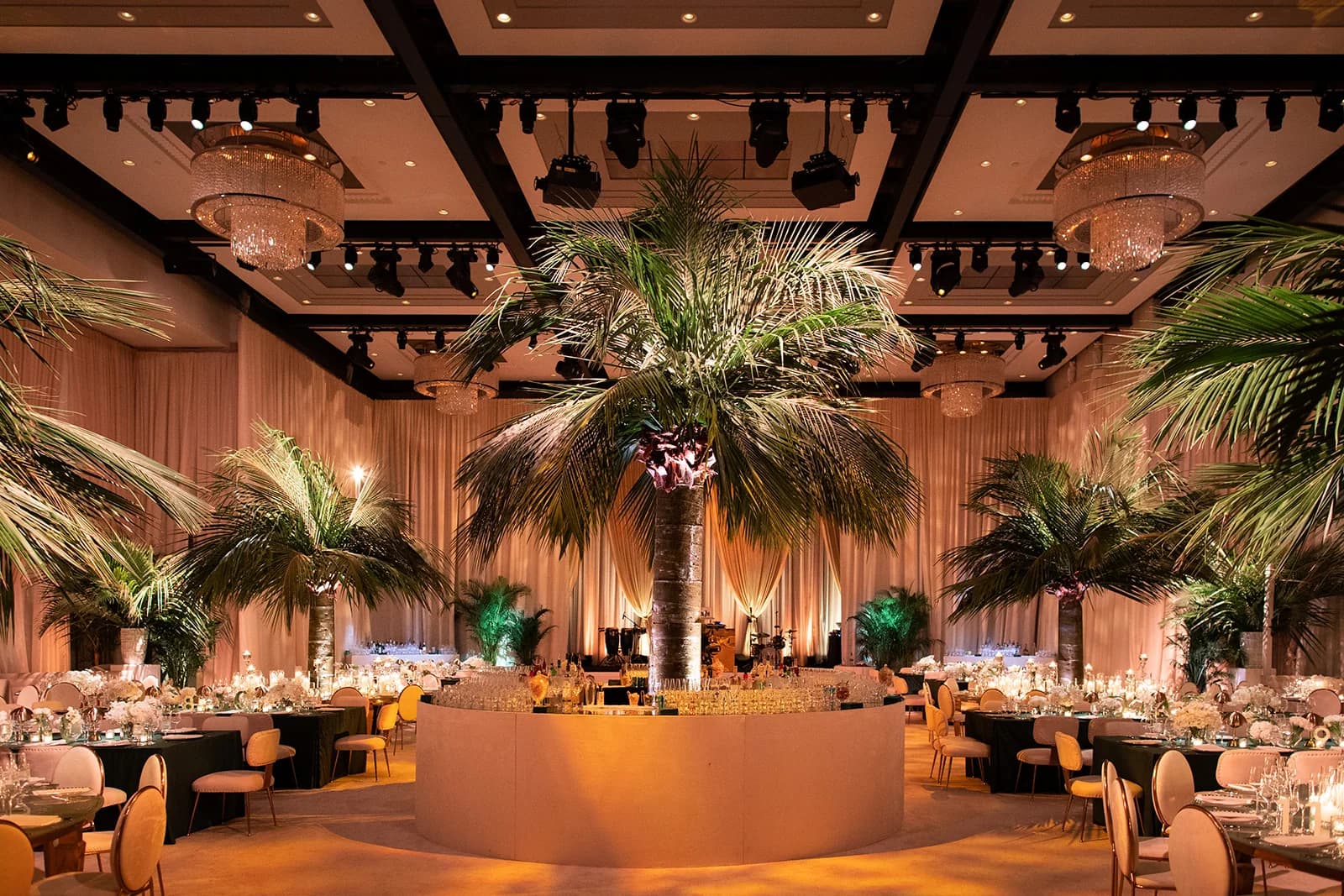 Palm filled ballroom with candlelit tables and gold lighting