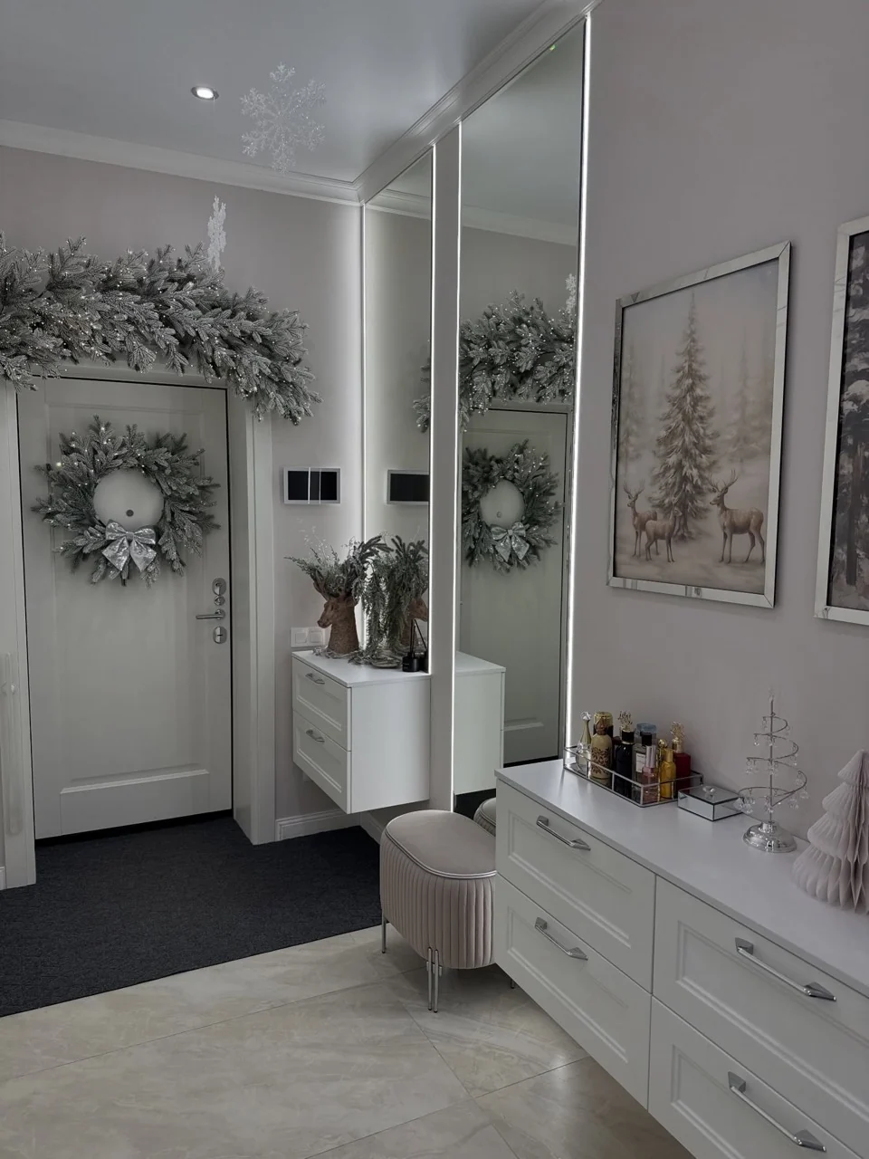 White entrance hall with a frosted wreath and matching garland above the door beside mirrored cabinets.