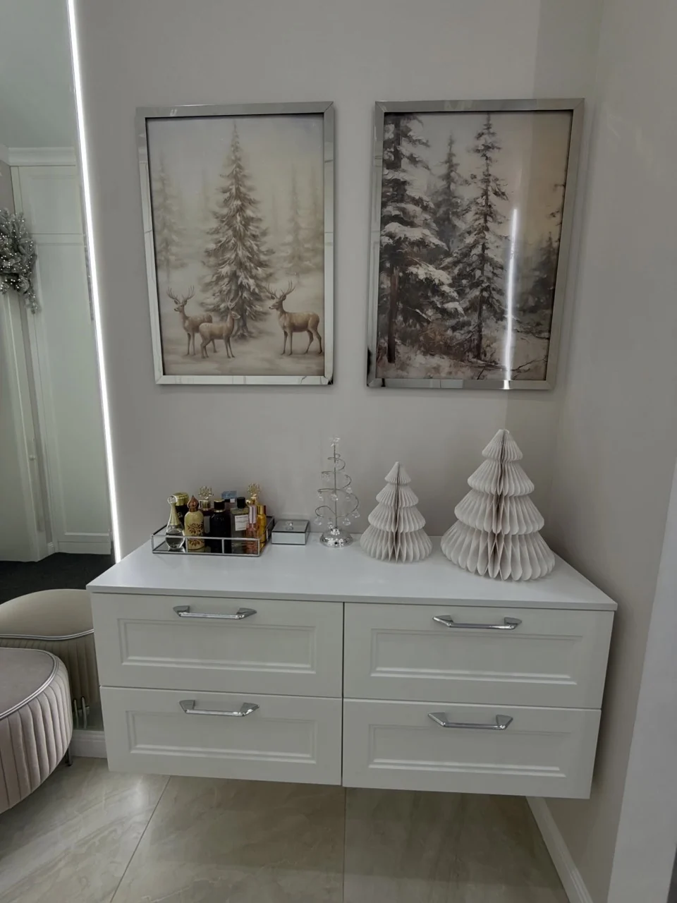 White honeycomb trees and a clear spiral tree on a wall-mounted console beneath framed winter woodland prints.