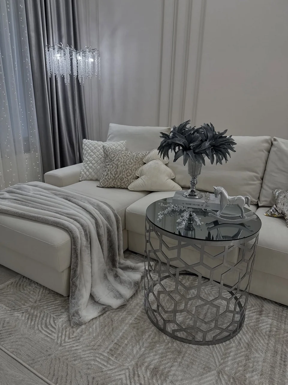 Cream sofa with winter cushions and a soft throw beside a mirrored table with a silver rocking horse and dark foliage arrangement.