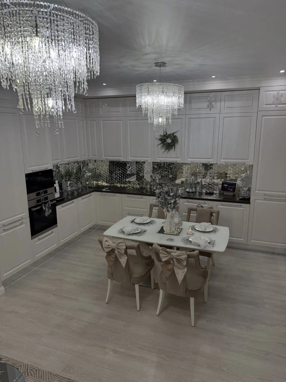 White kitchen and dining area decorated with silver accents, a festive table setting and large bows on dining chairs.