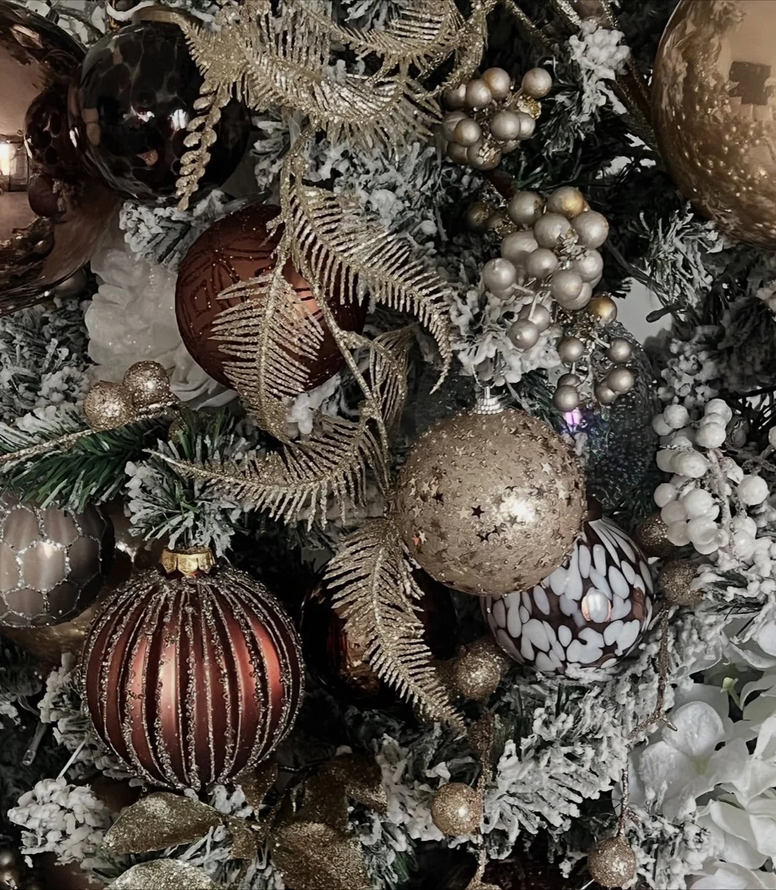 Close view of bronze and gold baubles, metallic fern sprays, pale berries and frosted Christmas tree branches.